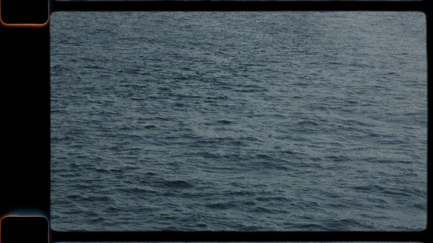 Vintage 8mm film captures a speedboat and other boats sailing across the sea on a hazy summer day