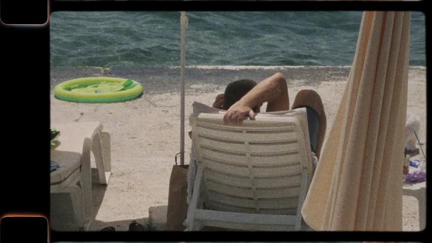 Vintage-style footage of a man relaxing in a beach chair and watching the waves on a sunny summer day
