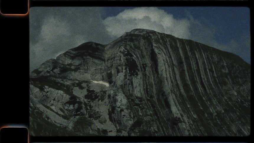 A vintage-style panning shot reveals the dramatic layered rock formations of a majestic mountain range