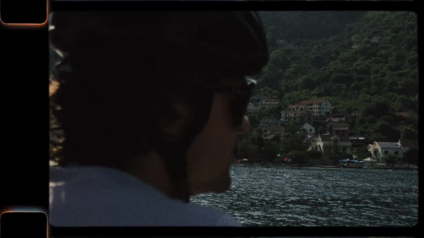 Vintage-style Super 8 footage shows a close-up of a cyclist in a helmet enjoying the scenic view of a beautiful European bay