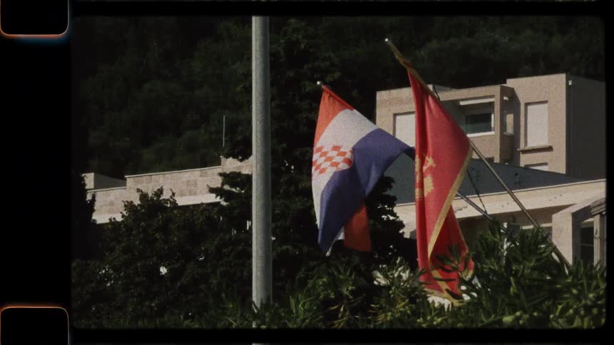 Vintage 8mm footage of the flags of Yugoslavia and the Socialist Republic of Croatia waving in the wind