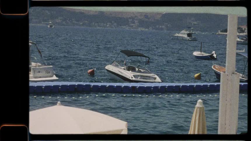 A vintage film captures boats and yachts gently swaying in the water of a sunny Mediterranean bay