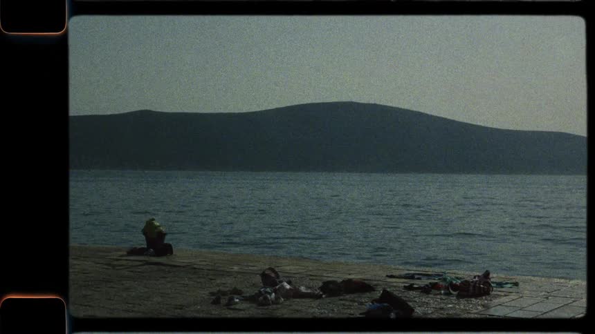 Vintage film captures a carefree summer day with people swimming and relaxing on a pier by a mountain-lined sea