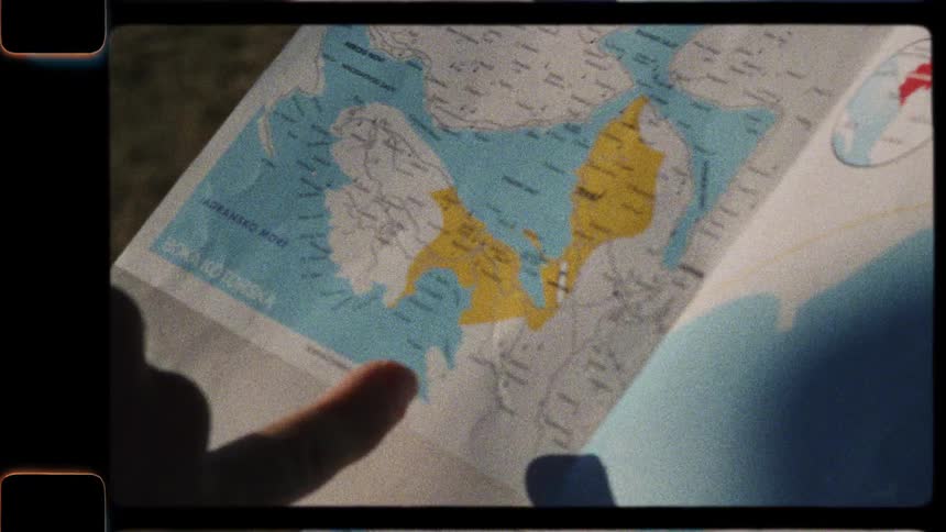 A traveler's silhouetted hand traces a path on a paper map in this vintage Super 8 film style clip