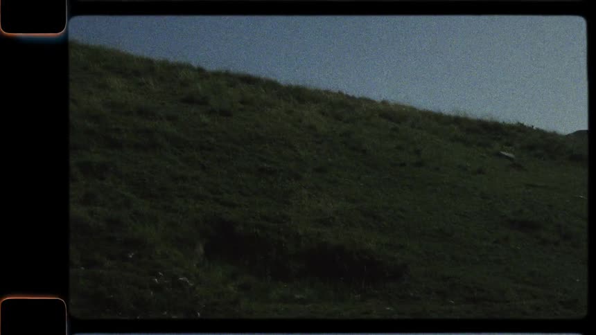 A nostalgic Super 8 film captures a slow pan across a dark mountain silhouette, revealing a lush green valley and a distant rocky range