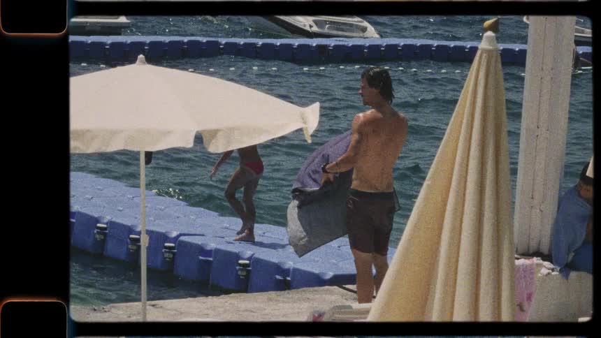 Vintage-style footage of a man climbing a ladder out of the sea onto a busy pier at a sunny resort
