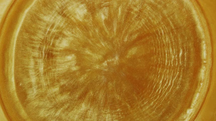 Hypnotic concentric ripples spread across the surface of a glittering golden fluid in a top-down view