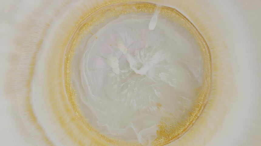 A pearlescent white bubble with a shimmering gold ring expands and morphs in a mesmerizing abstract display
