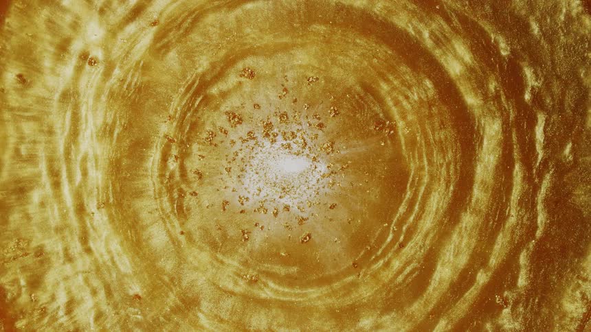 A mesmerizing top-down view of a hypnotic vortex of swirling golden liquid with shimmering glitter particles creating a beautiful abstract background