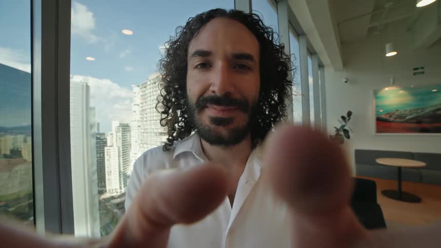 Cinemagraph of a smiling man holding a phone for a video call in a modern office with a city view