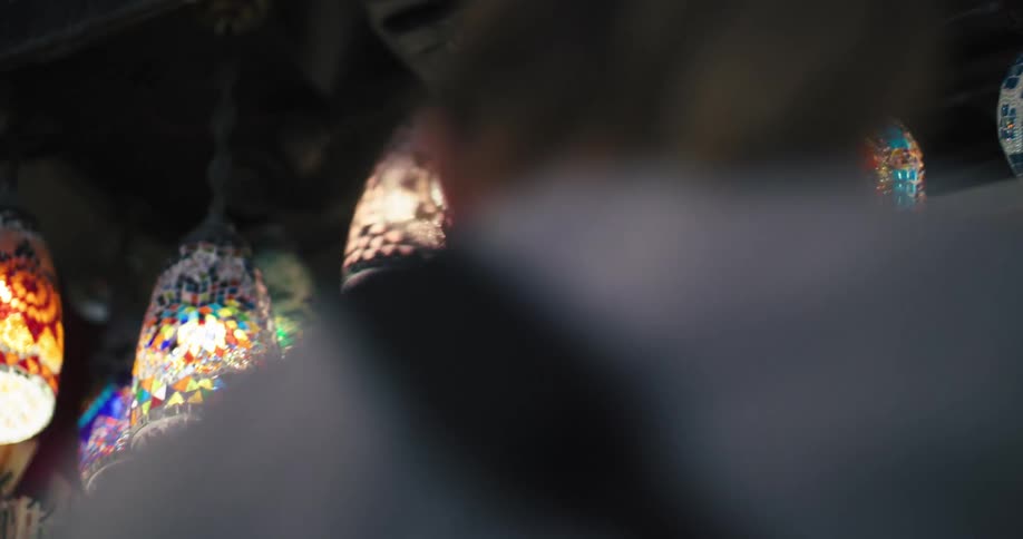 Colorful illuminated Turkish mosaic lamps hang for sale in a market stall in a slow motion pan