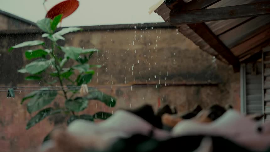 Raindrops fall in slow motion from a rustic roof gutter in a weathered backyard setting