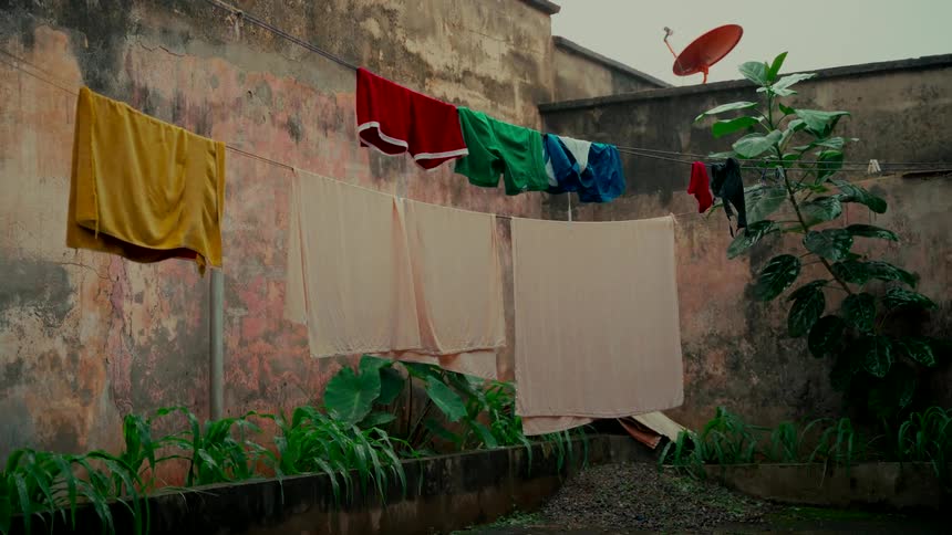 Colorful laundry hangs on a clothesline in a weathered urban courtyard during a rain shower