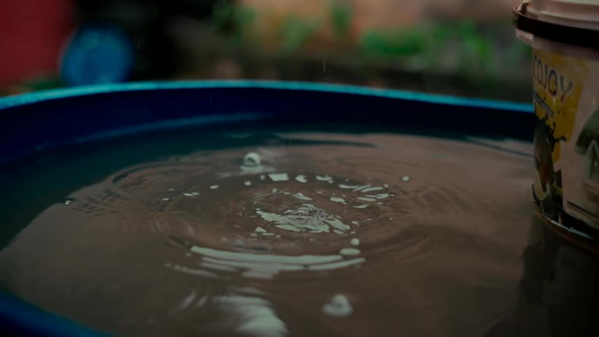 A close-up slow-motion shot of raindrops splashing into a blue basin filled with water, creating ripples on the surface
