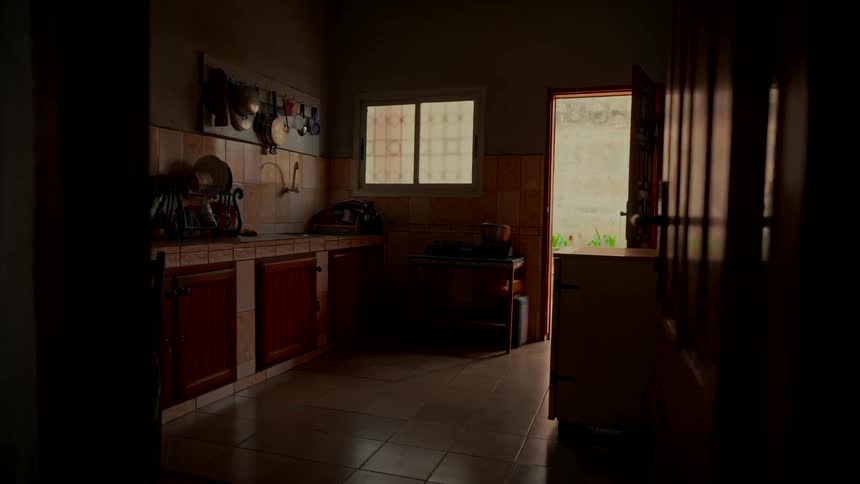 Sunlight streams through an open door into a dark and quiet rustic kitchen