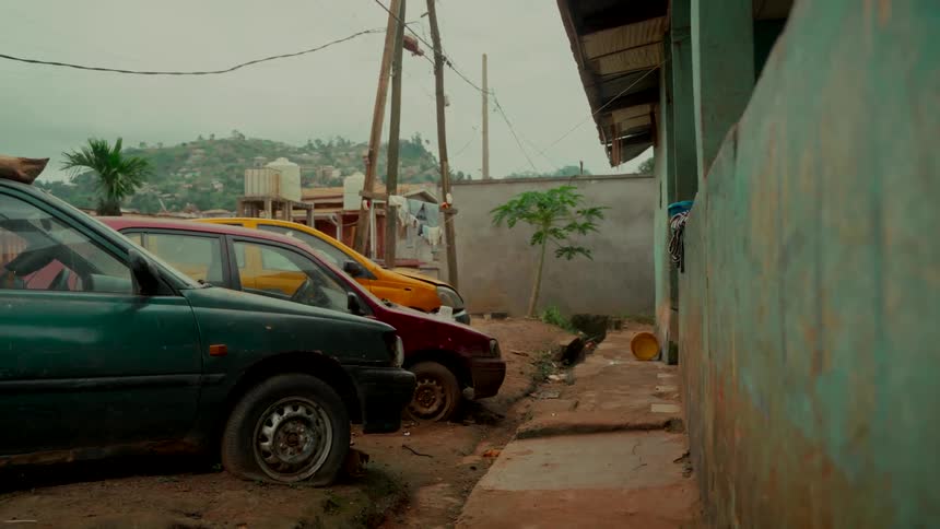 Old, abandoned cars with a flat tire are parked on a dirt road in a hillside village in Africa