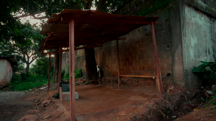 A quiet, empty, rustic bus stop with a corrugated tin roof stands in a rural village setting