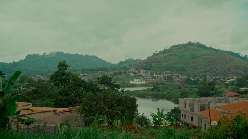 A serene view of a riverside village nestled among lush green hills on an overcast day