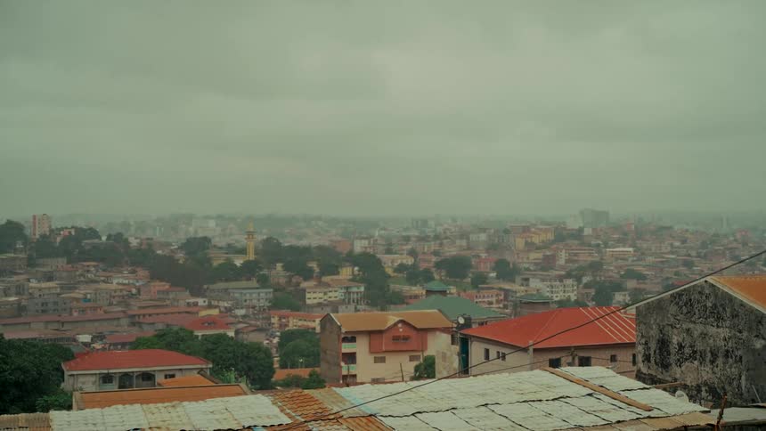 A wide, static shot captures the dense urban landscape of Yaoundé, Cameroon, under a gloomy, foggy sky