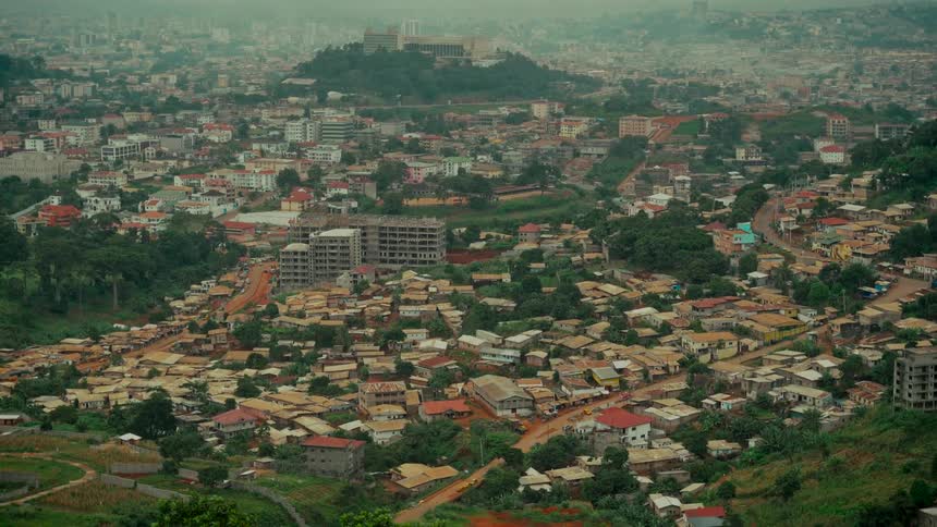 The capital city of Yaoundé in Cameroon spreads across rolling green hills under a hazy, overcast sky