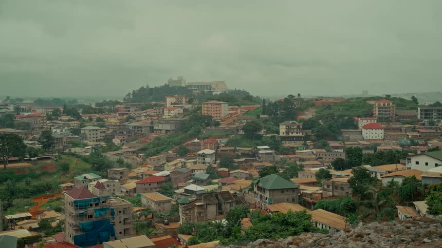 An expansive view of the sprawling city of Yaoundé, Cameroon, nestled among green hills under an overcast sky