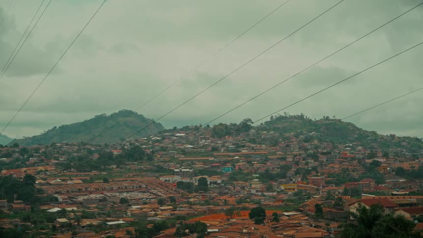 A wide shot shows a vast city built across rolling green hills under a cloudy sky, with power lines visible in the foreground
