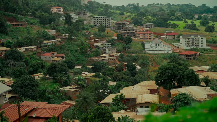 A wide, static view of a developing town with homes nestled in a lush green, tropical hillside