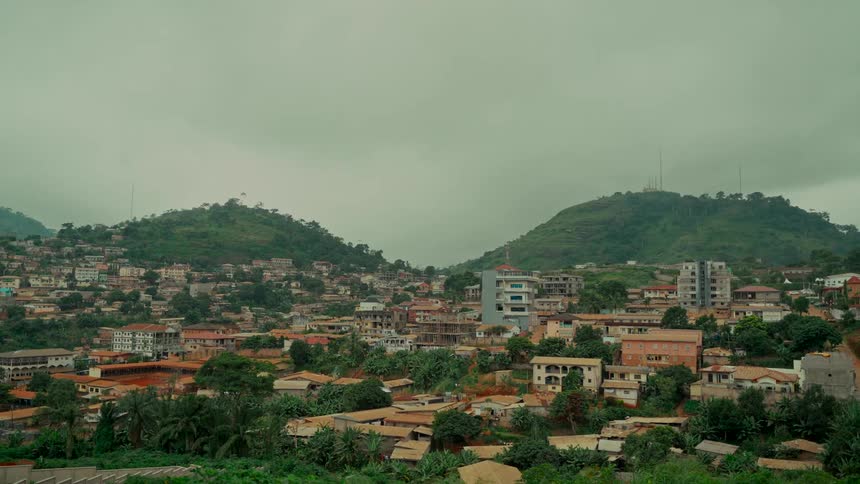 A wide, static shot of a city built into lush, green hills on an overcast day in a tropical region