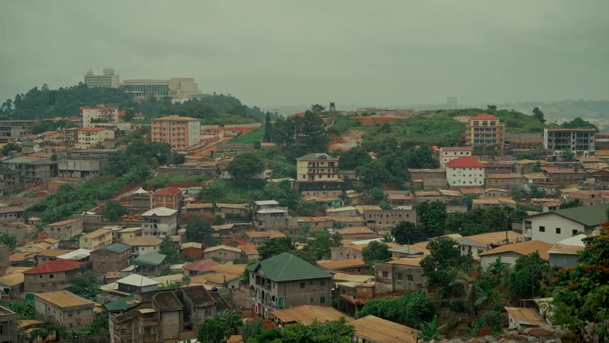 Establishing wide shot of a bustling city nestled in lush green hills on an overcast day