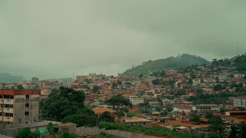 An expansive view of a city built into the side of a lush, green mountain on a cloudy day