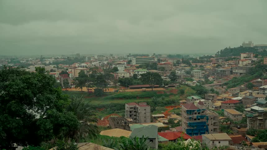 A static wide establishing shot of a sprawling city built on green hills under a gloomy, overcast sky
