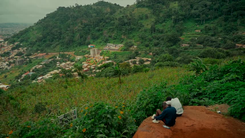 From a peaceful vantage point on a lush hillside, two young men look out over a city nestled amongst green mountains