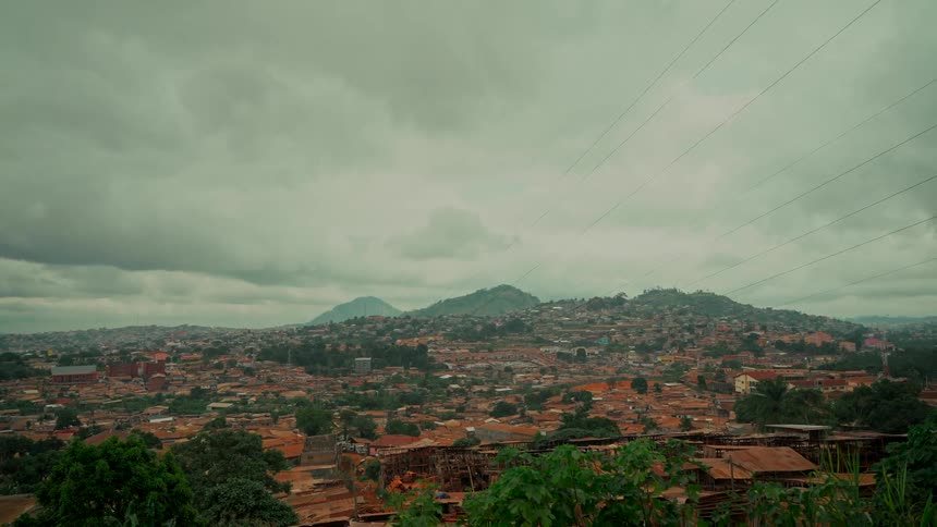 A sprawling hillside city with reddish-brown roofs sits under a thick blanket of grey clouds