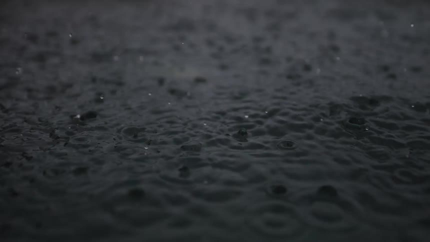 Heavy rain falls on dark water creating ripples and splashes in a slow-motion close-up