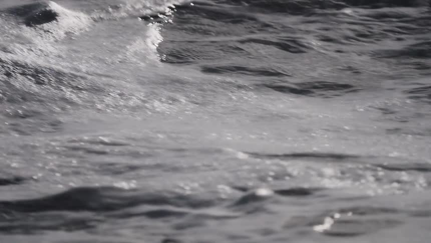 Gentle white sea foam slowly recedes in a mesmerizing slow-motion close-up, revealing the dark, sparkling ocean surface