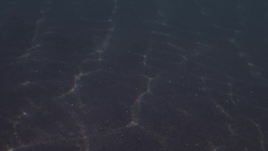 Gentle underwater shot of sunlight casting shimmering patterns on dark sand