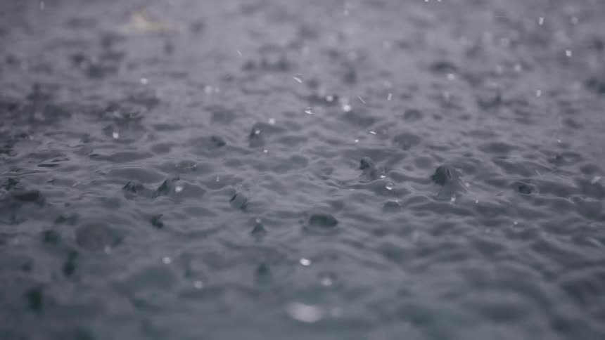 Mesmerizing slow-motion close-up of raindrops falling onto the surface of dark water, creating beautiful ripples