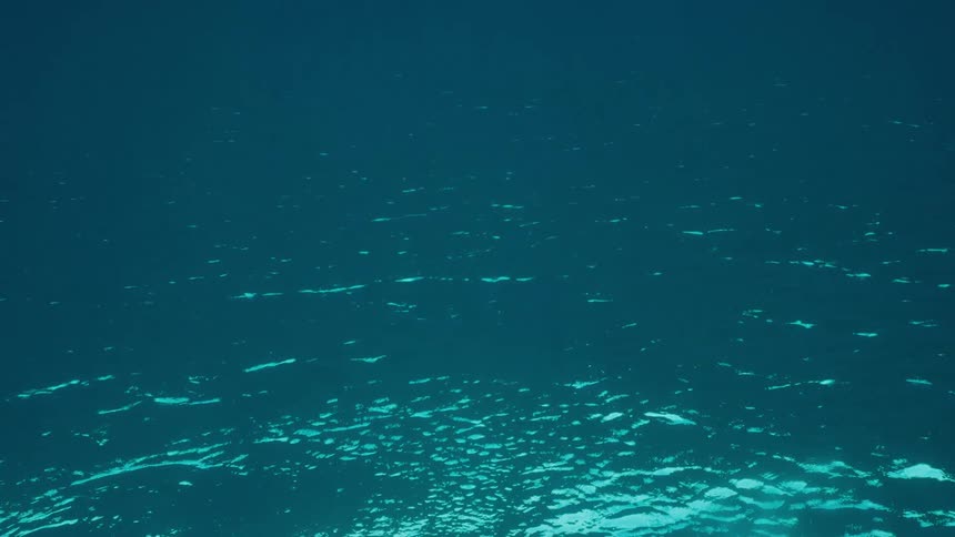 The calm, rippling surface of dark turquoise water creates an abstract and serene background