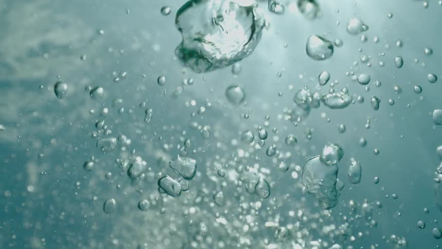 An underwater view of air bubbles rising towards the sunlit surface in slow motion