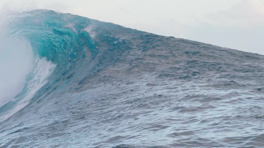 An impressive slow motion shot captures a massive turquoise ocean wave as it curls and breaks with immense power