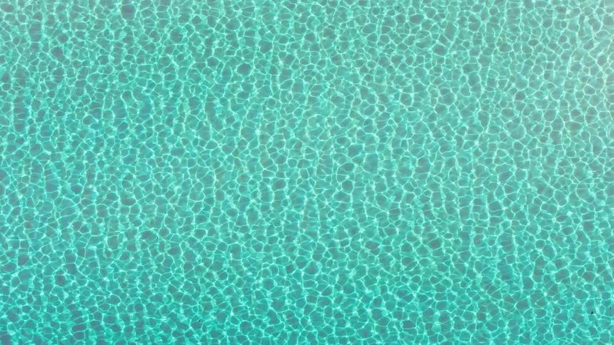 A serene aerial top-down view of shimmering, crystal-clear turquoise ocean water with sunlight creating caustic patterns