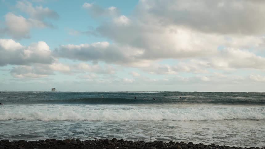 A slow-motion cinemagraph captures the serene beauty of ocean waves rolling in as surfers wait in the distance
