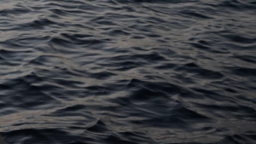 Dark, moody ocean water gently ripples and flows in a mesmerizing slow-motion close-up