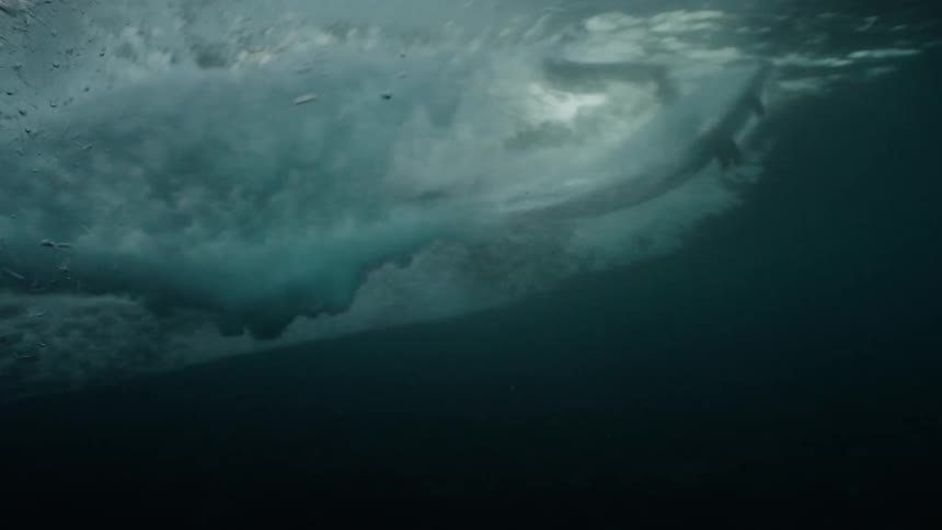 Slow motion underwater view of a surfer's board gliding across the water's surface