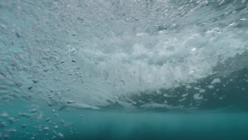 An immersive underwater slow-motion view of a powerful ocean wave breaking over a surfer and their surfboard