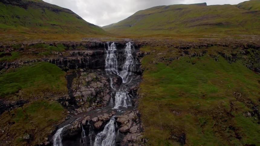 Water flows down a green and rocky waterfall