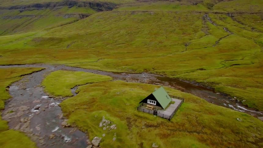The long green field has a single house in the middle