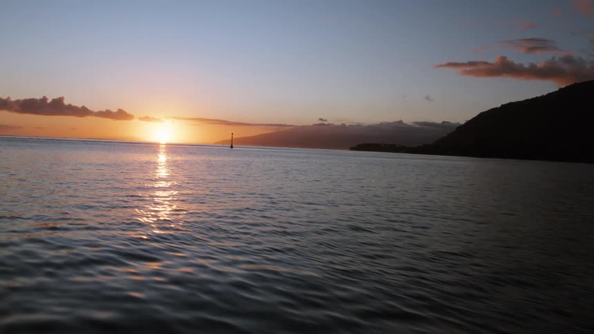 A serene ocean view at sunset with gentle ripples on the water and a distant island silhouette on the horizon