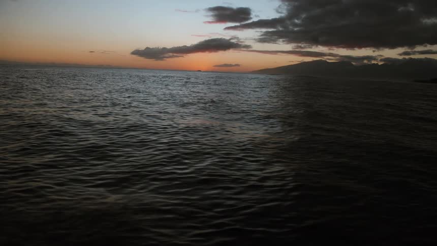 A moody sunset over a dark, rippling ocean with the silhouette of a distant island on the horizon