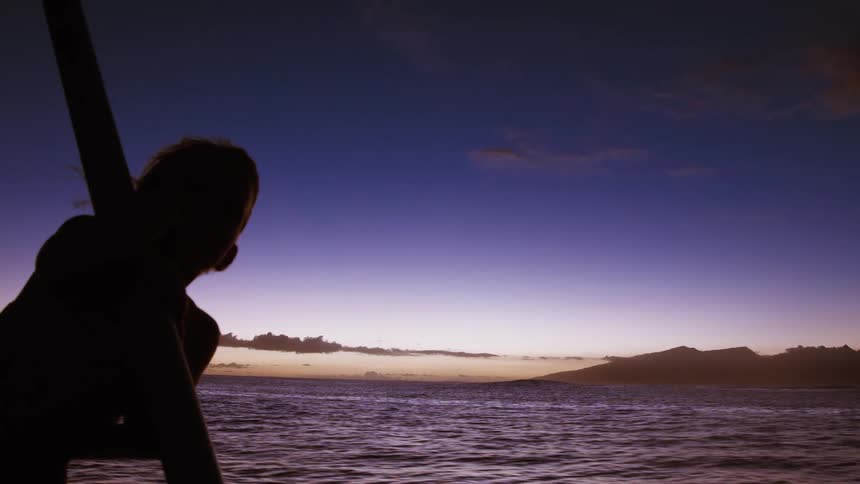 A silhouetted woman peacefully watches the purple twilight sky over a tranquil ocean